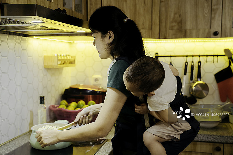女人在厨房做饭，用吊带将婴儿绑在身上图片素材