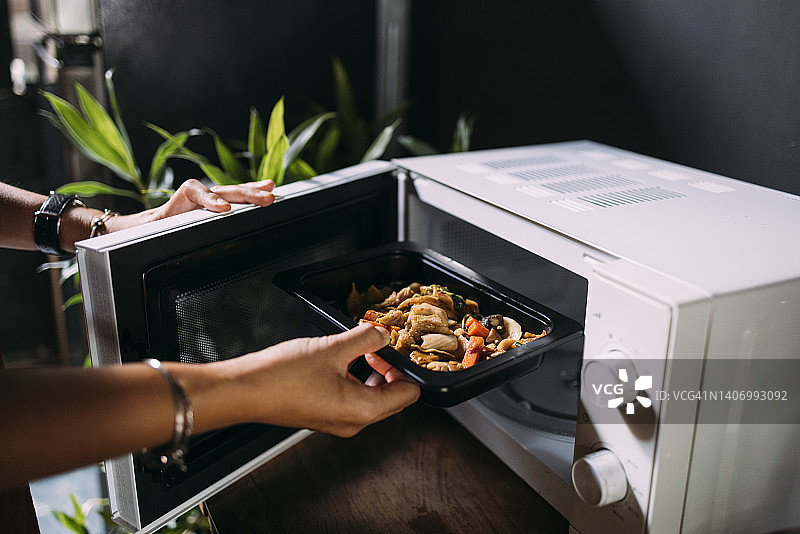 匿名白人女性在烤箱里加热食物的裁剪照片图片素材