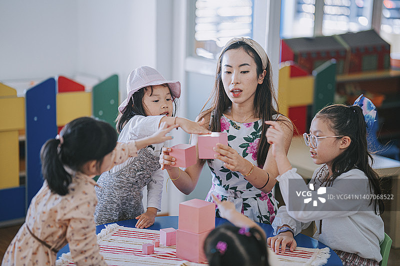 亚洲幼儿教师在教室里指导学生用积木搭建塔图片素材
