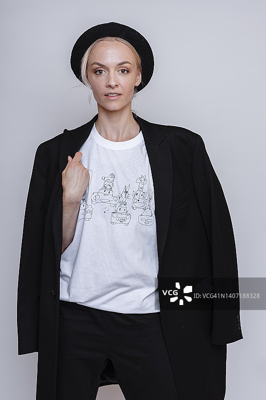 戴着软呢帽的时髦女性在灰色背景的影棚中摆姿势，优雅自信地看着镜头图片素材