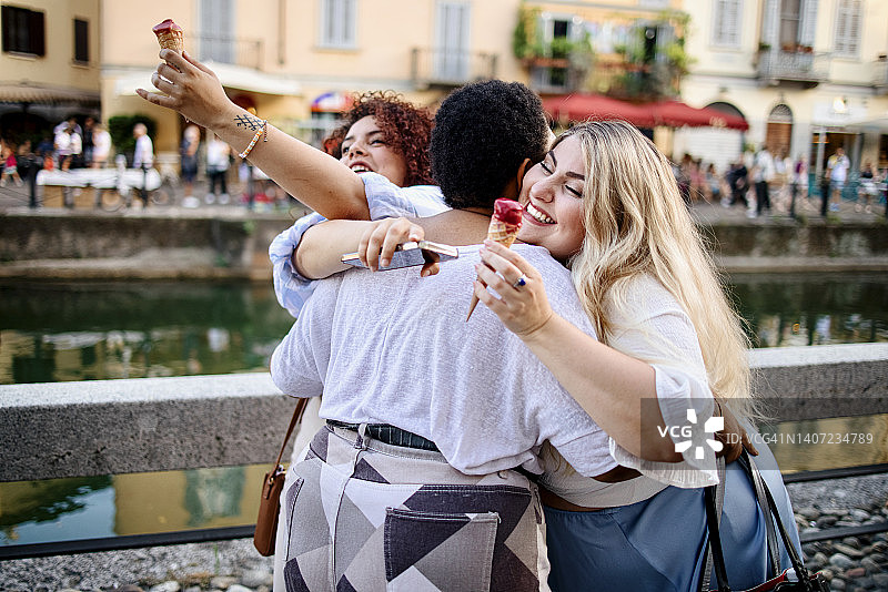 三个欣喜若狂的多种族女性朋友拥抱在一起，很高兴在户外见面图片素材