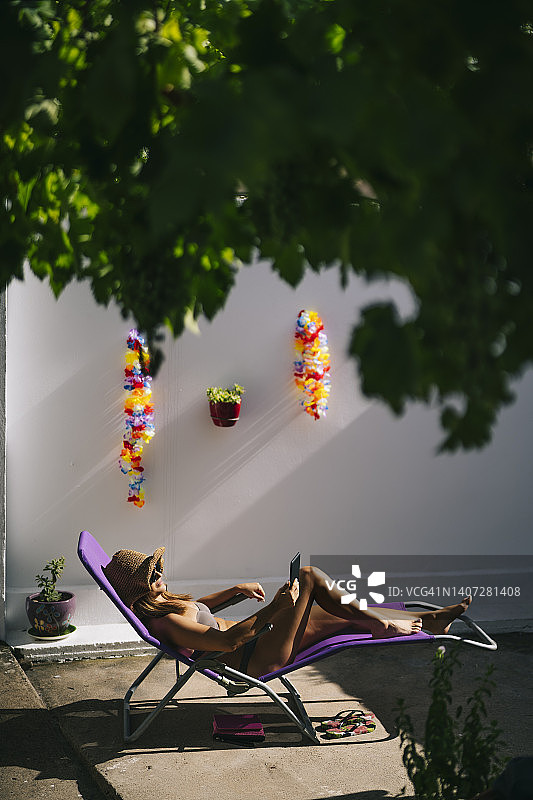 戴着帽子和太阳镜在自家露台上日光浴和阅读的女人图片素材