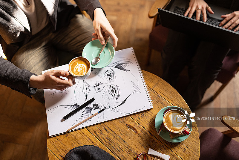 在咖啡馆使用笔记本电脑的都市青年男人和绘画的女人图片素材