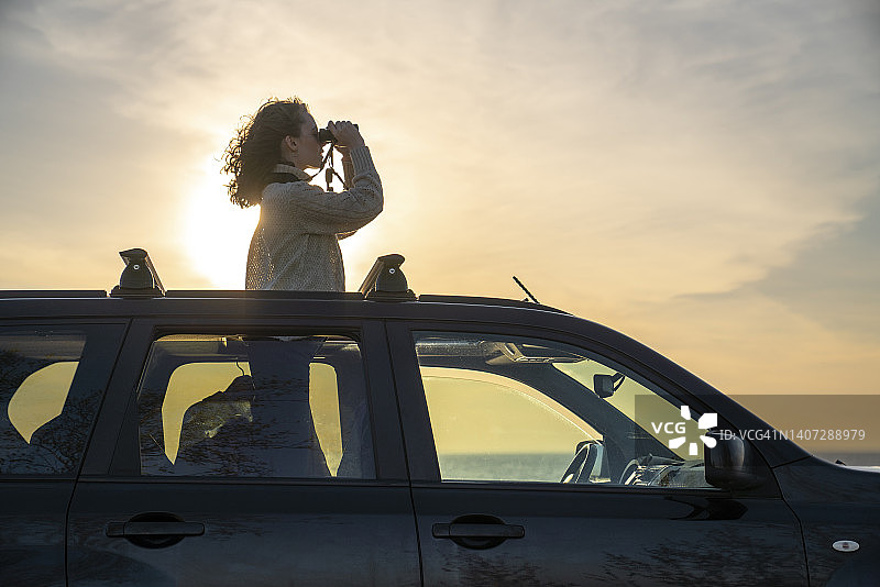 年轻女子在日落时分用望远镜观看图片素材