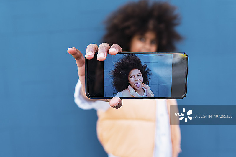 在智能手机屏幕上看到的女孩伸出舌头的自拍图片素材