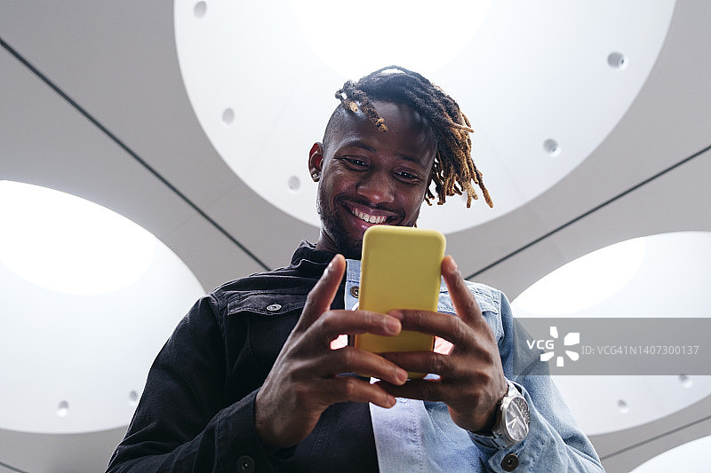 在照明天花板下使用智能手机的微笑男人图片素材
