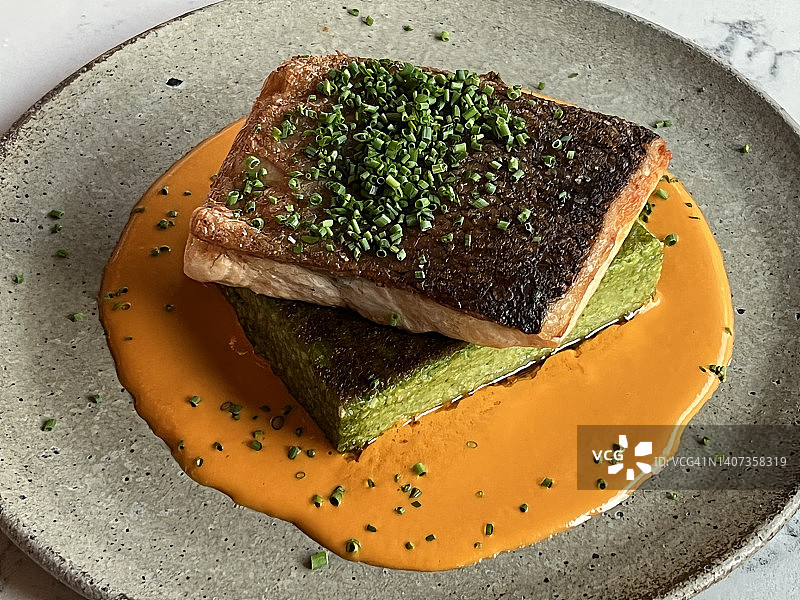 一份精致的海鲜鱼片，配以红辣椒奶油酱，搭配蔬菜和奶油酱图片素材