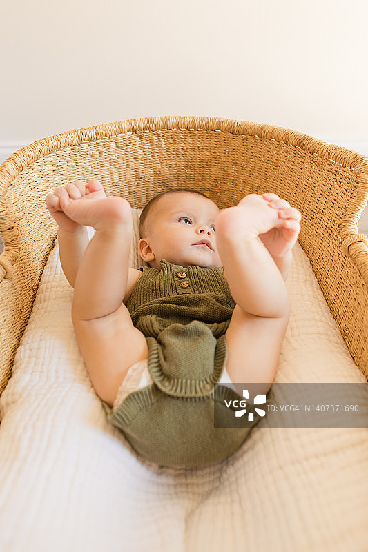 快乐的男宝宝穿着连体衣躺在篮子里微笑图片素材
