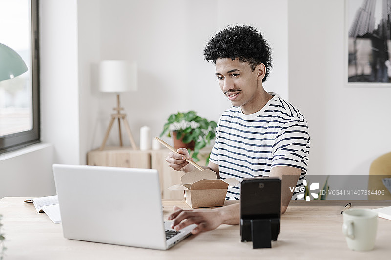 年轻男人边吃中餐边看笔记本电脑图片素材