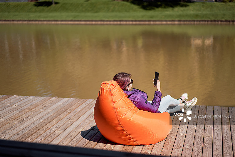 在乡间小屋湖边用手机休息的女人图片素材
