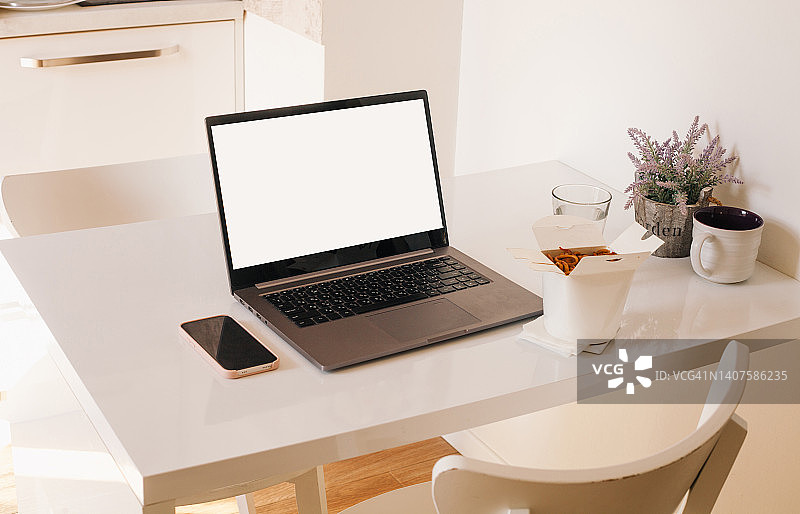 桌子上的笔记本电脑、手机和外卖面条：居家内景，自由职业和在家工作概念图片素材