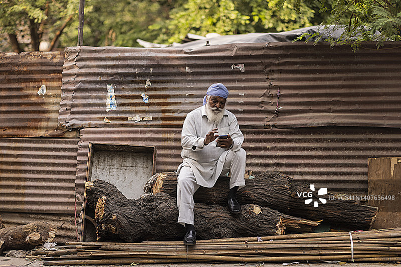 坐在木头上使用手机的年长男人图片素材
