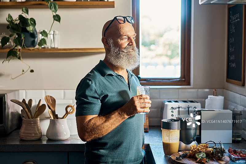 年长的男人用搅拌机喝健康的冰沙，注重健康的退休人员喝新鲜的有机果汁，每天混合蔬菜和水果的日常饮品，以改善健康和福祉图片素材