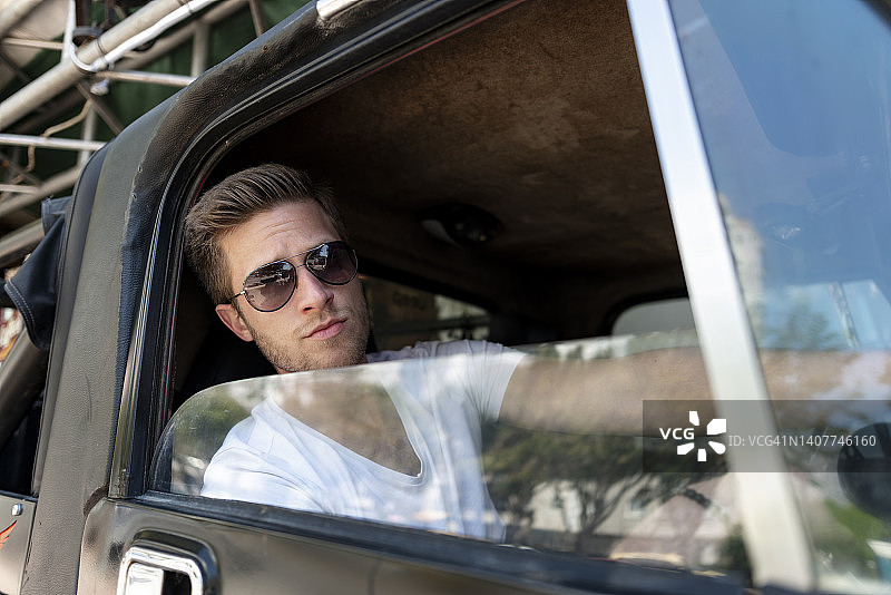 在SUV内的留着胡茬、戴着太阳镜的英俊金发年轻男子图片素材