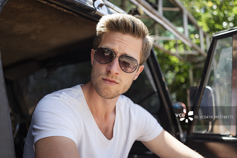 留着胡茬、戴着太阳镜的金发年轻男子站在黑色SUV前图片素材
