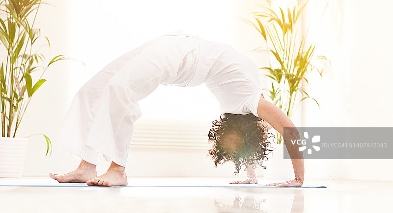 在禅修静修室课堂上做后弯轮式瑜伽姿势和伸展背部的女人图片素材