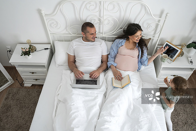 夫妻在床上，男人用笔记本电脑工作，女人读书图片素材