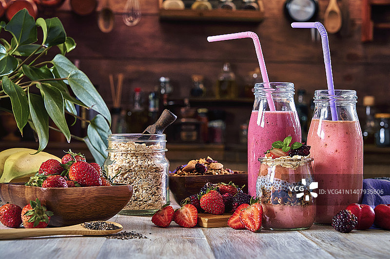 纯素食品主题。一套三种香蕉黑莓和草莓冰沙，配以谷物，装在带吸管的瓶子里，放在乡村风格的桌子上。图片素材