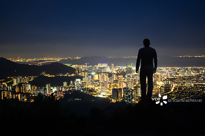 夜晚，男人背对镜头眺望城市夜景图片素材