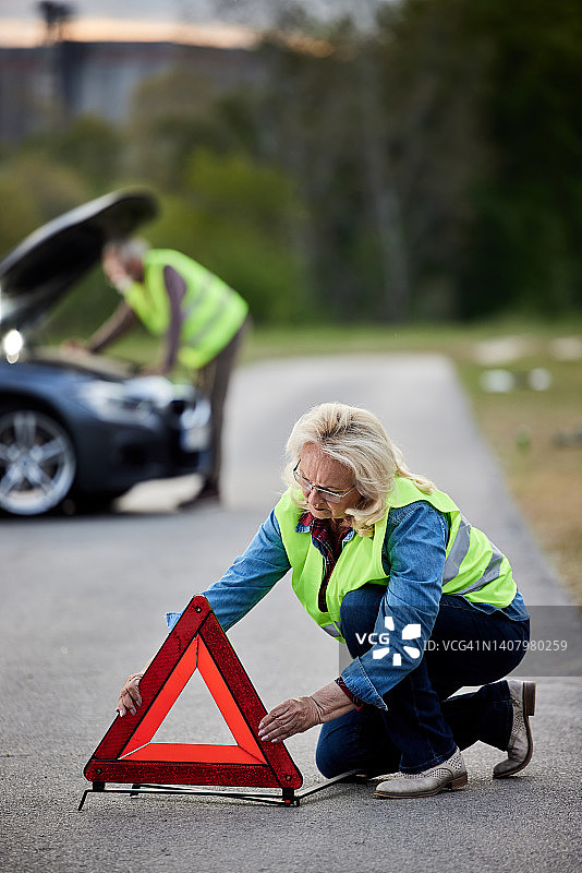 年长的女人在车辆故障后放置交通警告标志图片素材