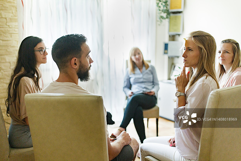 在团体治疗期间围成一圈坐着的男人和女人，额头上有便利贴图片素材