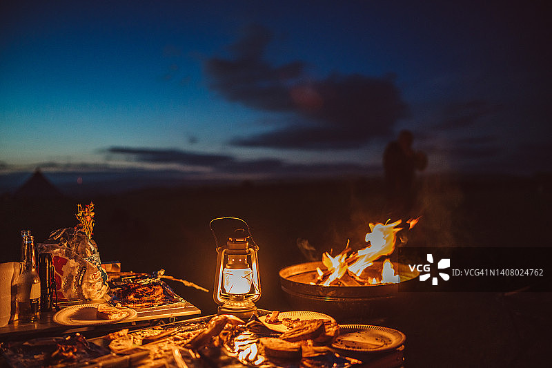 露营桌上的食物和油灯，旁边是燃烧的篝火图片素材