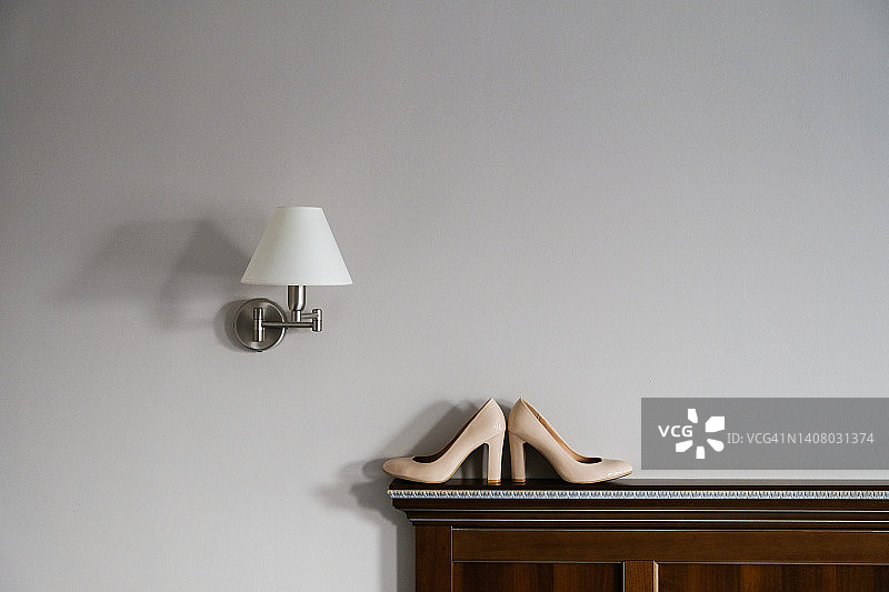 阳光明媚的日子里，新娘的设计师结婚鞋放在靠墙的木架上。采用真皮制成的新款现代时尚女士高跟鞋。婚礼的早晨准备工作图片素材