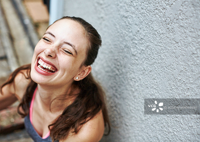 年轻女子坐在户外靠墙，因幸福或幽默而大笑图片素材