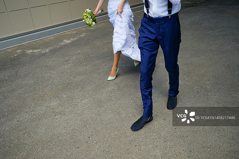 新娘和新郎走在城市街道上，新娘手捧美丽的白色鲜花和绿叶。婚礼当天，仪式，户外。图片素材