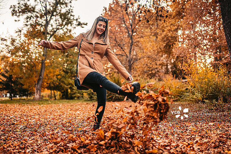年轻女人踢一堆树叶图片素材