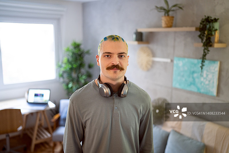 在房间里自豪地站着的染发胡须的都市年轻男人肖像图片素材