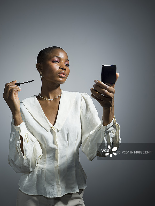 年轻漂亮女模特用粉饼镜涂睫毛膏图片素材