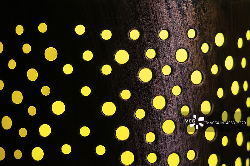 亮黄色背景下带有不同尺寸孔的圆柱形金属图片素材