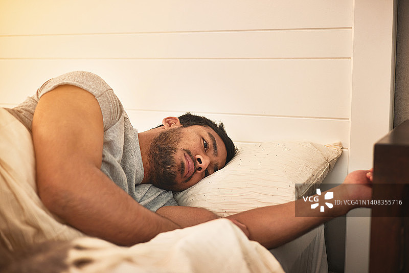 失眠的早晨，悲伤沮丧的男人在床上醒来。一个年轻人正与精神健康问题作斗争，情感破裂和人际关系困难图片素材