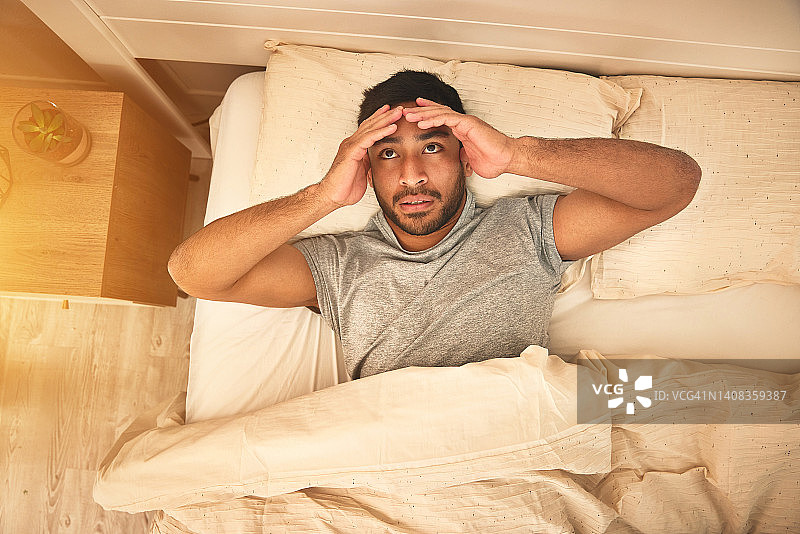 一个年轻男人头痛地躺在卧室里，感到疲惫和沮丧图片素材