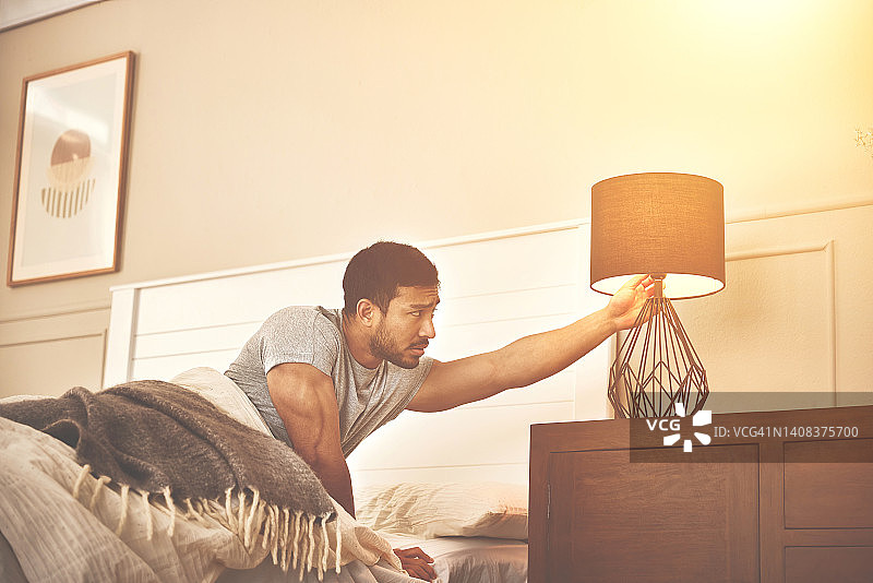 男子失眠，彻夜难眠后精疲力竭，清晨醒来。倦怠和压力导致精力不足和睡眠不足。在一天结束时关掉一盏灯图片素材