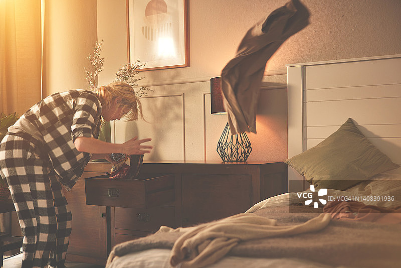 睡过头后急忙穿衣服的焦虑女性。一个穿着睡衣的年轻女性在抽屉里寻找衣服，因为她上班要迟到了。沮丧的女人匆忙扔衣服图片素材