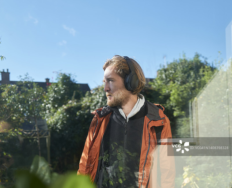 窗外花园里戴耳机的橙夹克男人图片素材