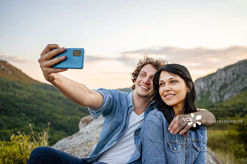 幸福情侣坐在山顶上，以美丽的风景自拍图片素材