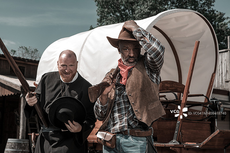 帅气黑人牛仔与牧师在狂野西部背景中图片素材