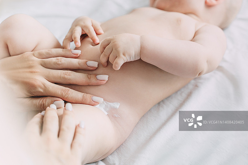 母亲在婴儿的尿布下涂抹尿布疹膏图片素材