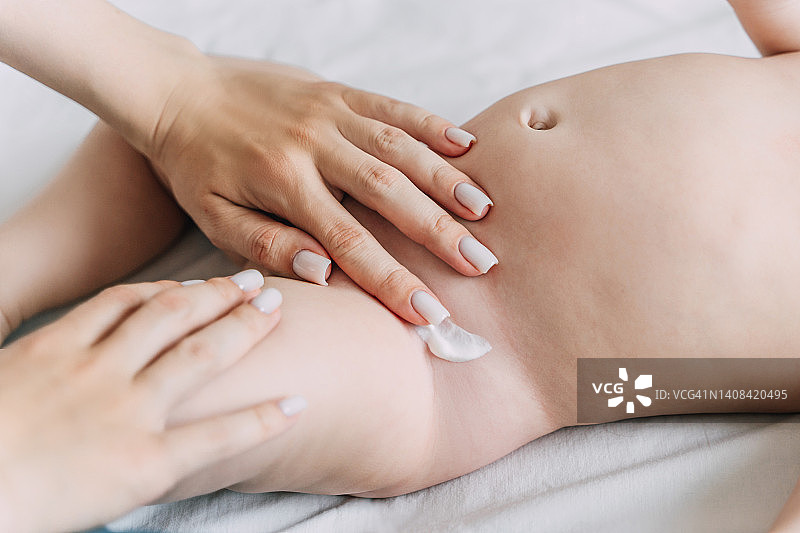 母亲在婴儿的尿布下涂抹尿布疹膏图片素材