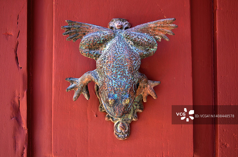 红色木门上的青蛙/蟾蜍形黄铜门环图片素材