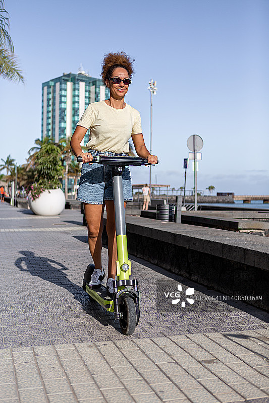 快乐的女人在堤坝上骑电动滑板车图片素材
