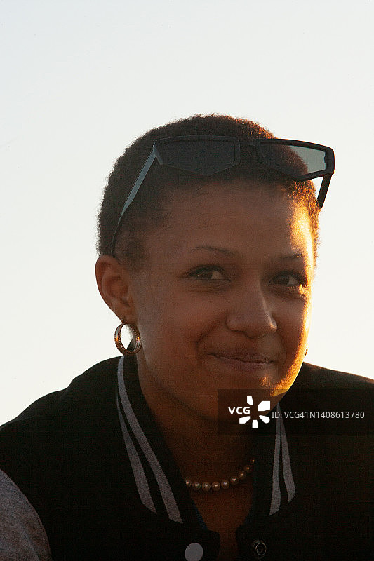 戴着复古或未来主义黑色太阳镜的少女，阳光照在她半边脸上，带着微笑的表情看着镜头图片素材