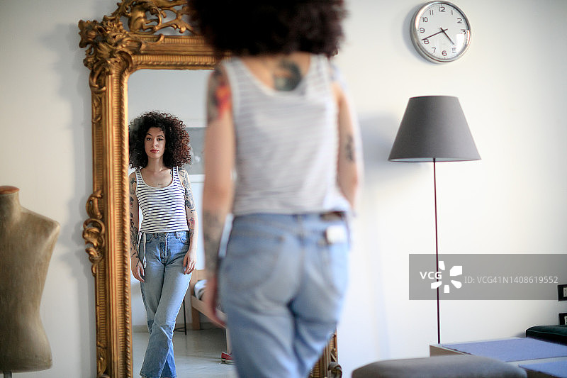 在家照镜子的年轻棕色卷发纹身女子图片素材