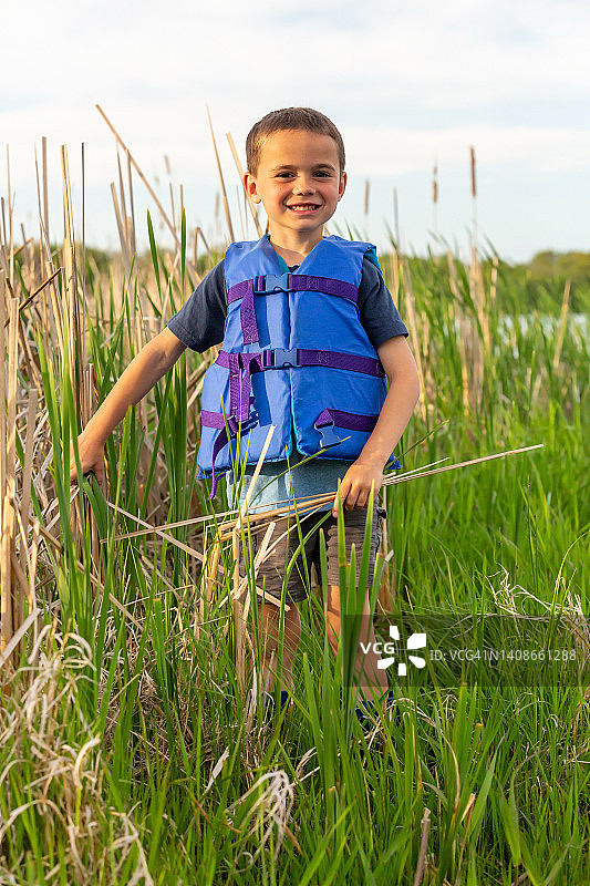 男孩穿着救生衣走过香蒲芦苇图片素材
