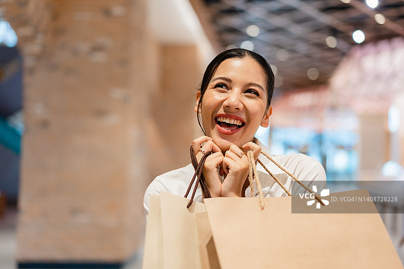 快乐的亚洲年轻女人在城市购物中心购物图片素材