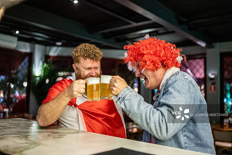 在酒吧里边交谈边喝啤酒的运动迷朋友图片素材