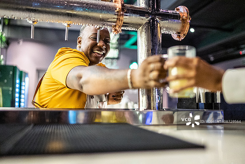 年轻女服务员在酒吧给顾客供应啤酒图片素材